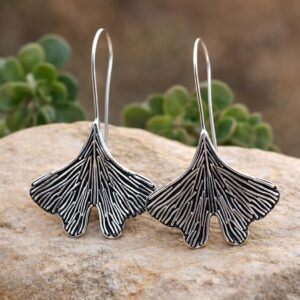 Boucles d'oreilles pendants Ginkgo Sünya en laiton argenté patiné posées sur une pierre.
