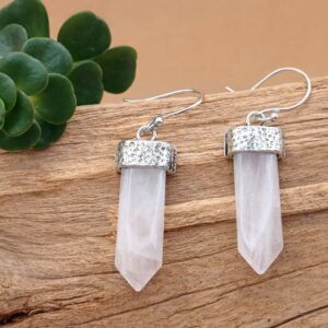 Gros plan d'une oreille portant une boucle d'oreille Sünya en laiton argenté avec pointe de pierre de lune facettée.