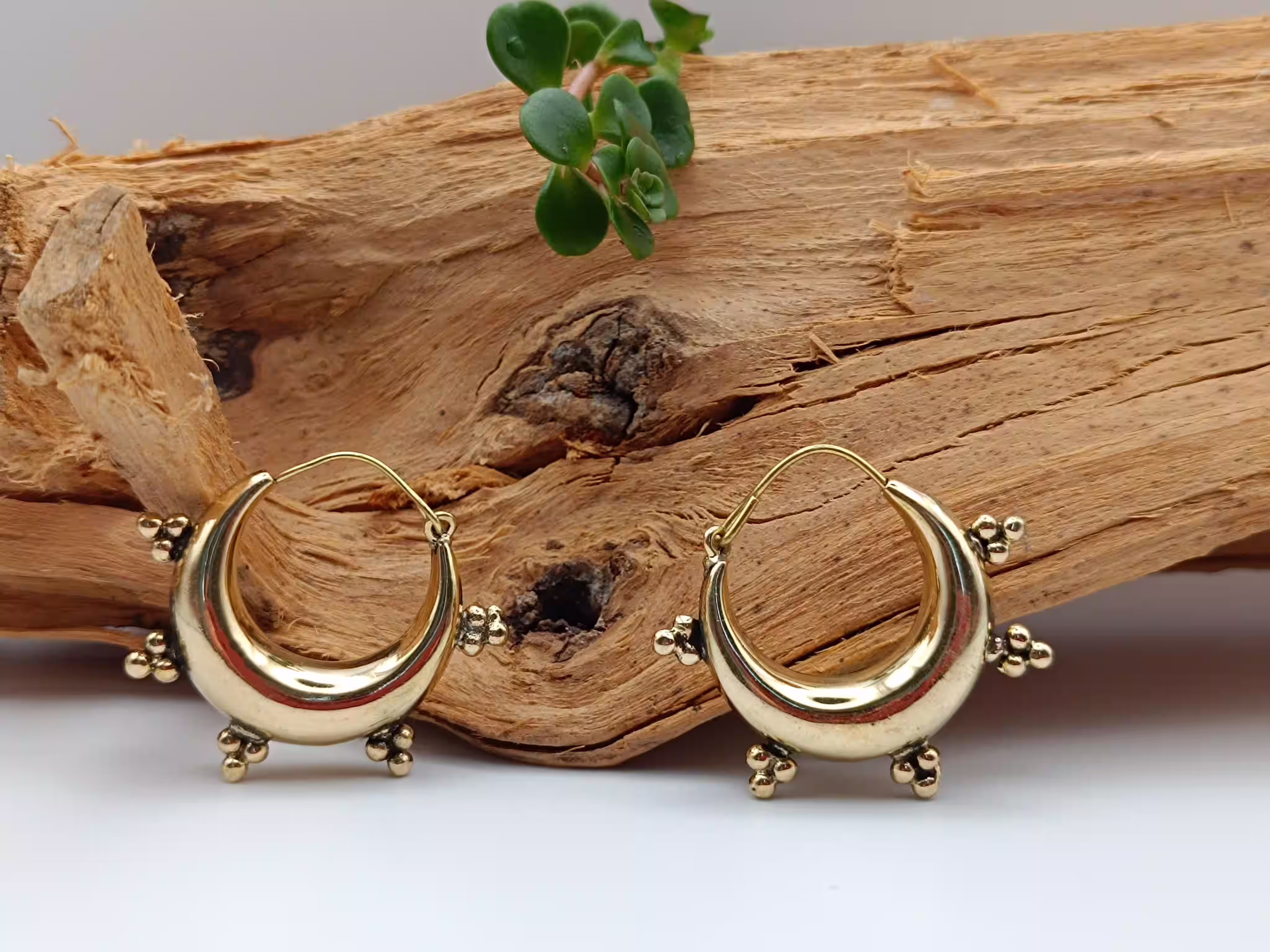 solia-boucles-oreilles-ethniques-laiton-doré Paire de boucles d'oreilles créoles épaisses en laiton doré de style ethnique, posées sur un bois brut.