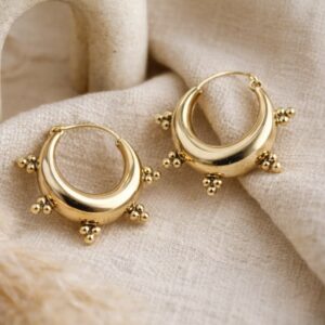 Paire de boucles d'oreilles créoles épaisses en laiton doré de style ethnique, posées sur un bois brut.