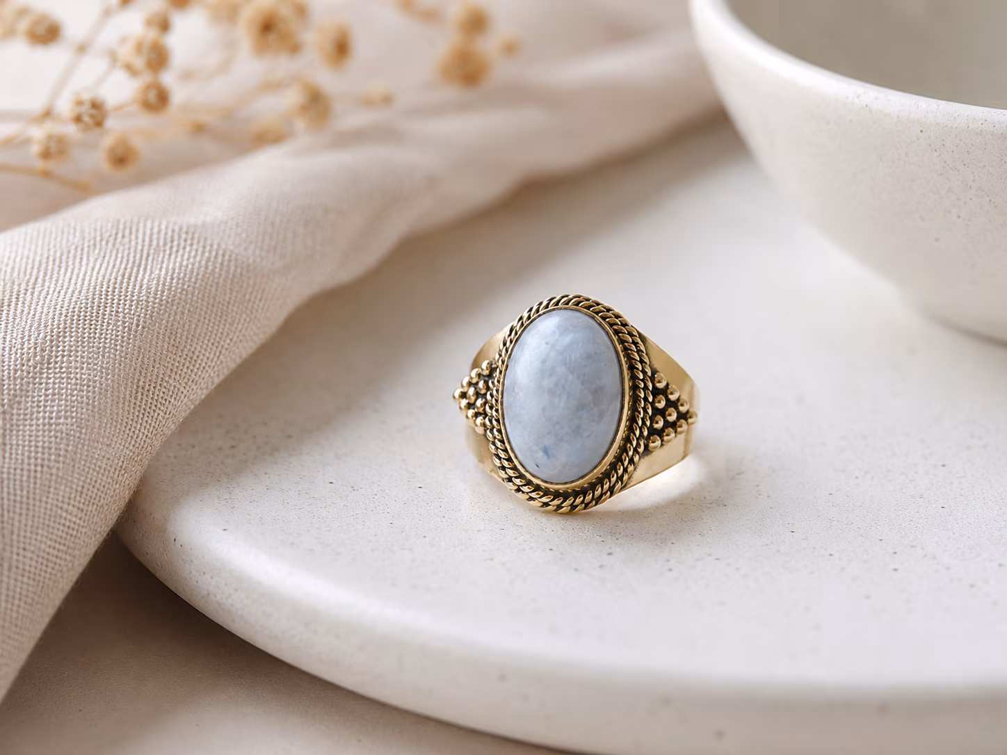 bague-large-laiton-lolia-details Bague en laiton pierre de lune modèle Lolïa posée sur une coupelle blanche.