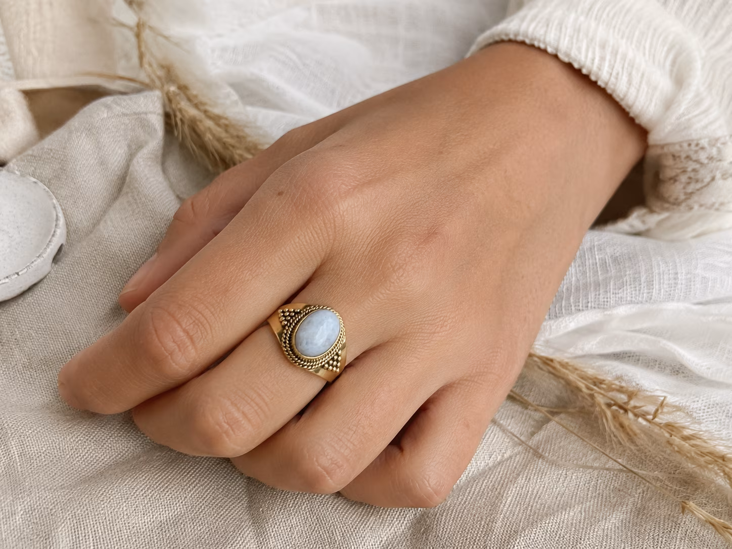 bague-laiton-pierre-de-lune-portee Bague en laiton pierre de lune Lolïa portée au doigt sur tissu en lin.