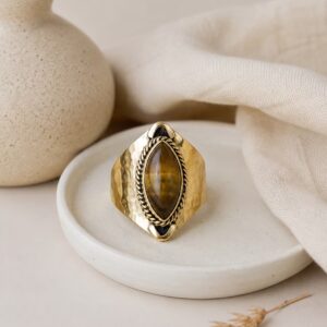 Bague en laiton martelé Salä avec pierre œil de tigre posée sur un support en céramique.